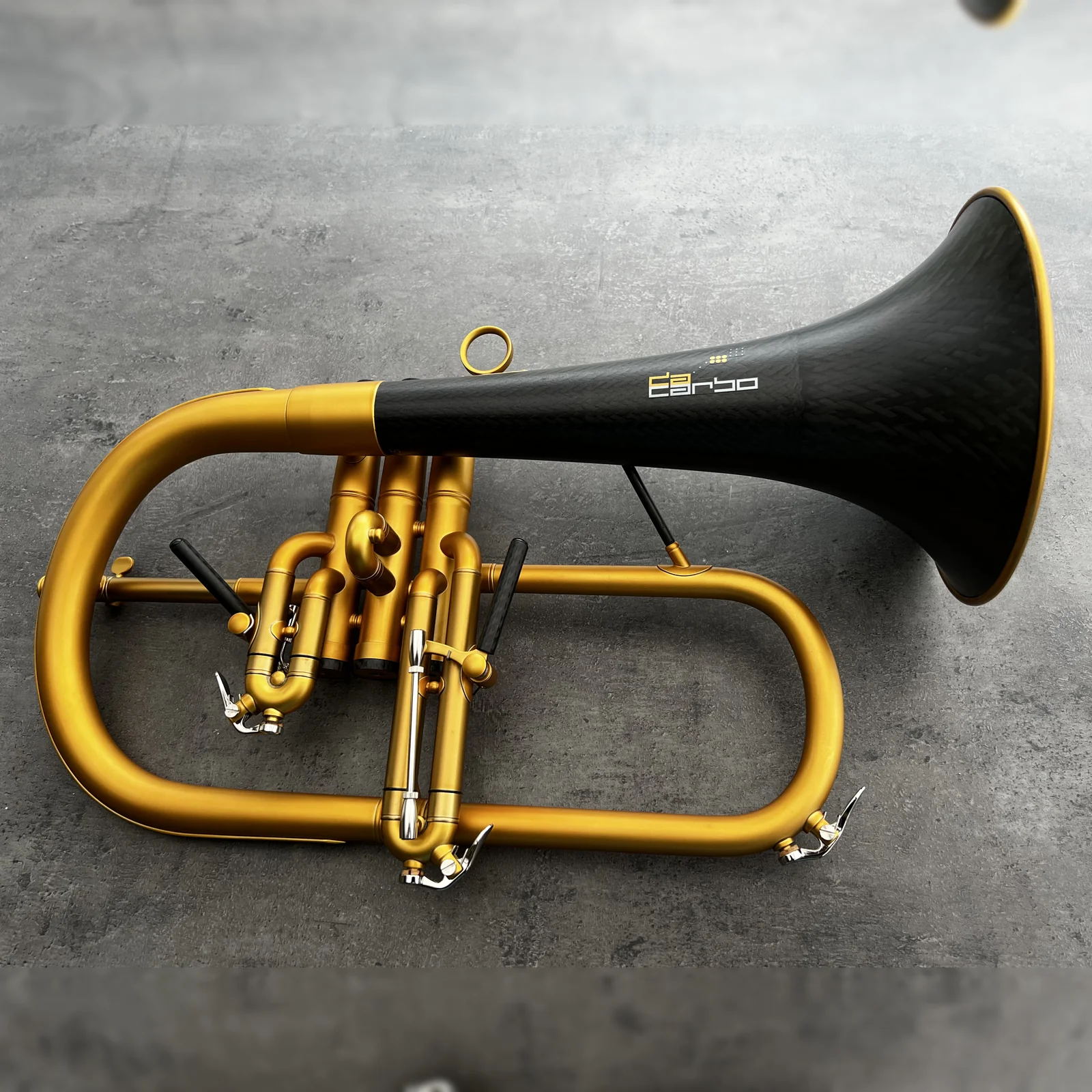 Ein daCarbo Fluegelhorn mit mattgoldenem Korpus und schwarzem Carbonbecher auf grauem Stein.